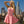 Load image into Gallery viewer, A blonde woman poses on a rooftop with the Los Angeles skyline in the background. She wears the Latex Swing Dress by Syren Latex in pink. The dress has tanktop sleeves and is form-fitting in the torso, and flares out at the waist.
