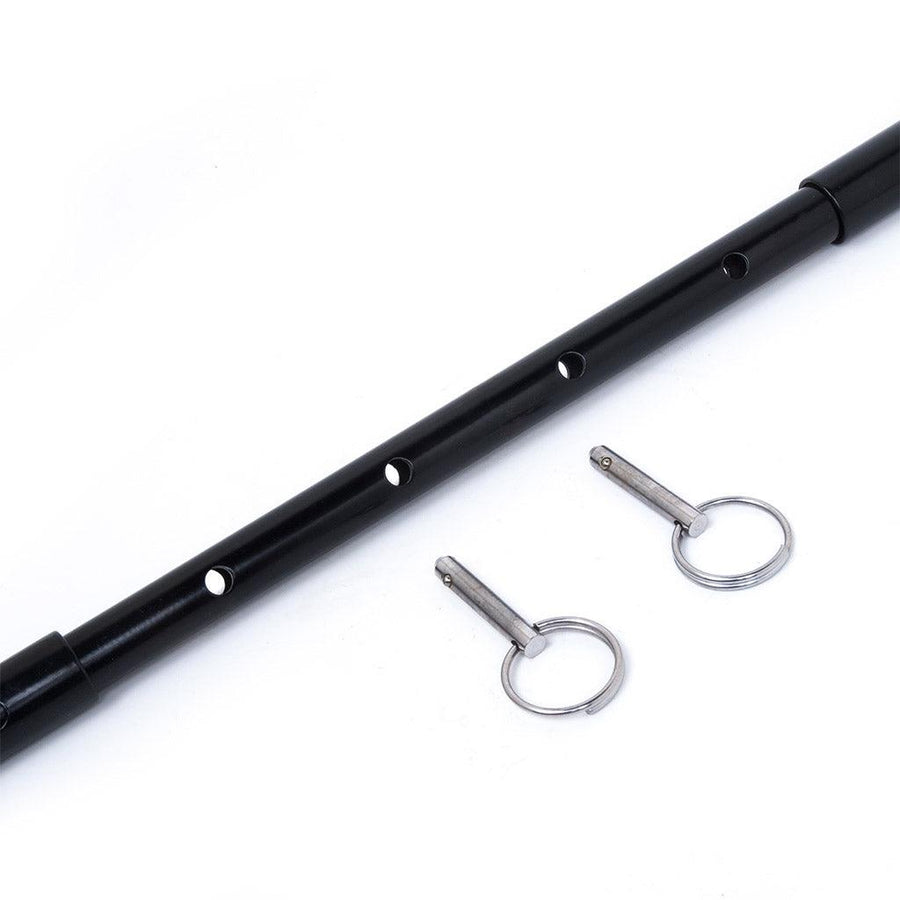 A close-up of the center of the black Adjustable General Purpose Spreader Bar is shown against a blank background. The pins are removed, and the hollow outer bars have been slid apart, revealing another bar with four holes that the pins can be placed in.