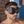 Load image into Gallery viewer,  A close-up of a brunette man with light facial hair is shown. He wears the black Mistress Heather Leather Blindfold, which has cupped eye covers with a small metal D-ring between the eyes.
