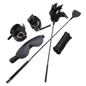 The contents of the Bondage 101 Kit are shown against a blank background. Laid out is a pair of wrist and ankle cuffs, a blindfold, rope, a feather tickler, and a riding crop. All of the items are black.