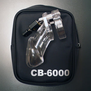 The assembled chastity cage is shown resting on top of the CB-6000 Package Male Chastity Kit case. The zipper case is made of black fabric with “CB-6000” in white on the bottom. 