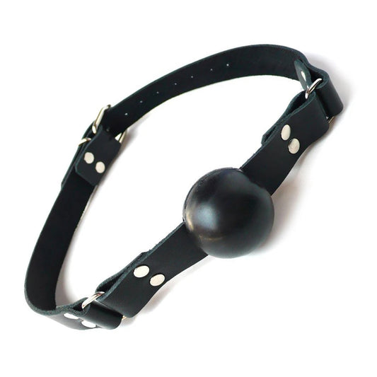 The black rubber ball gag is displayed against a blank background. It is a matte black rubber ball attached to a black leather strap with silver hardware, which buckles behind the head.
