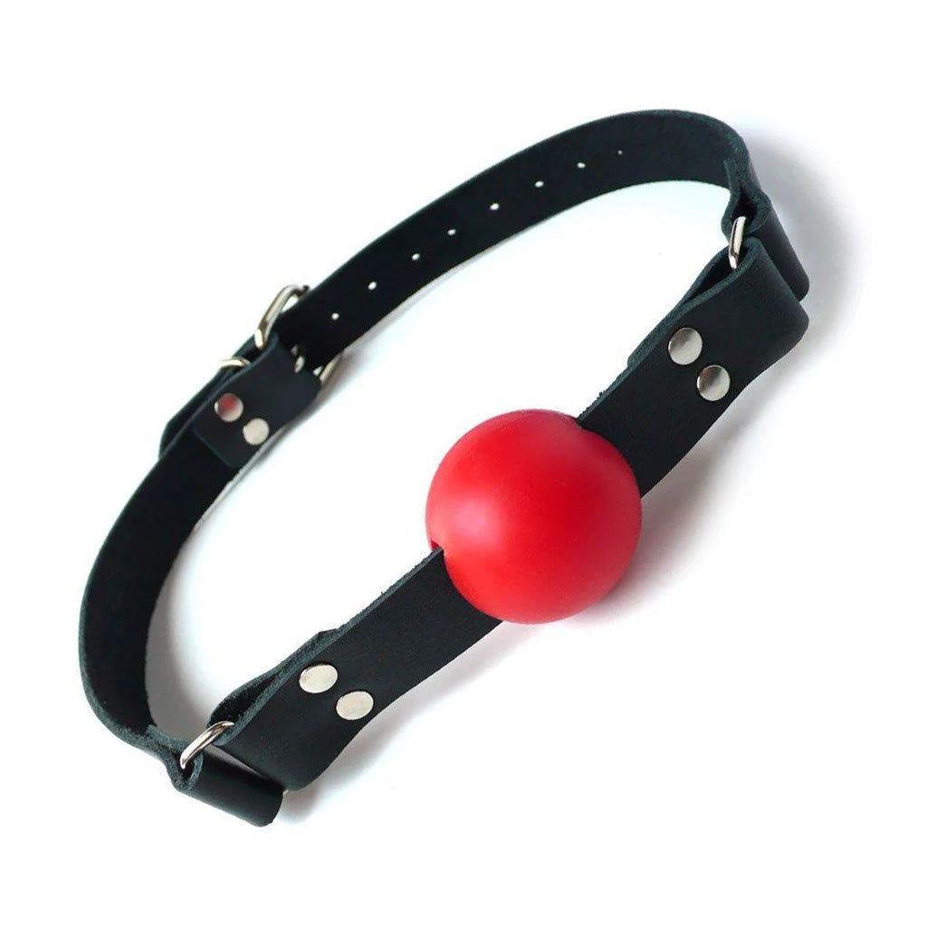 The red rubber ball gag is displayed against a blank background. It is a matte red rubber ball attached to a black leather strap with silver hardware, which buckles behind the head.