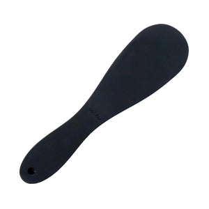 The Tantus Pelt Paddle, a matte black silicone rounded paddle with a curved handle, is displayed against a blank background.