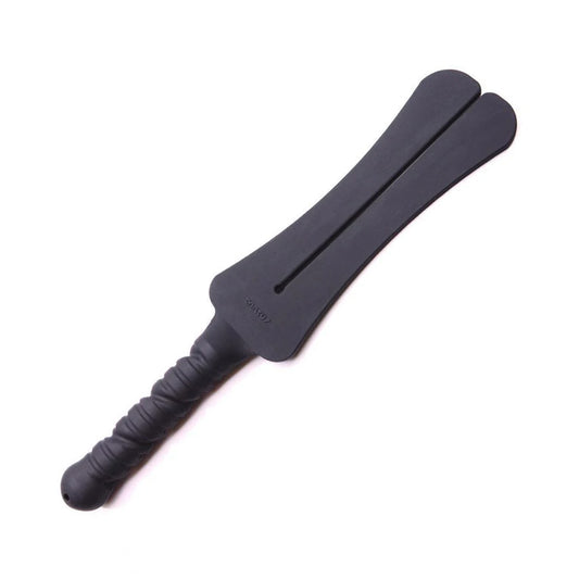 The Tantus Trip 2 Tawse Silicone Paddle is displayed against a blank background. It is made of matte black silicone. The handle is rounded and textured with a small hole at the bottom.