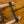 Load image into Gallery viewer, A close-up of a woman’s wrists is shown against a wooden floor. Her wrists are locked in the black Big Barrel 12 Inch Wrist Spreader Bar With black buckling Cuffs. A heavy black chain is connected to a D-ring in the middle of the spreader bar.
