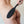 Load image into Gallery viewer, A close-up of a woman’s bare butt and back is shown in front of a white wall. Somebody is holding the black Tantus Gen Mini Silicone Paddle against her butt.
