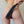 Load image into Gallery viewer, A woman’s bare ass is shown. She is standing in front of a white brick wall with her legs apart, and a hand is shown holding the black Tantus Silicone Mini Tawse on her ass. It is made of matte black silicone and is shaped like a paddle but split in half.
