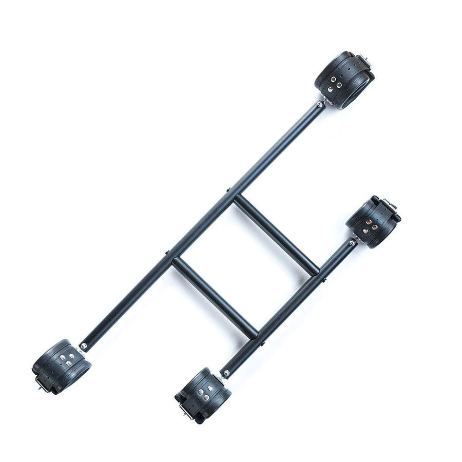 The Deluxe Pranger Pillory 4-Point Spreader Bar is shown against a blank background. It has two horizontal metal bars, one with wrist cuffs on each end and one with ankle cuffs. The two horizontal bars are connected by two vertical metal bars.