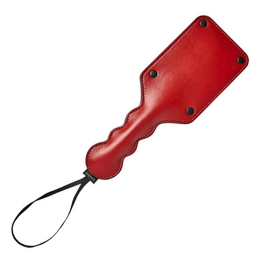 The Saffron Square paddle, made of red faux leather, is displayed against a blank background. The paddle is rectangular with rounded edges, and the handle has a bubble design with a wrist loop at the end.
