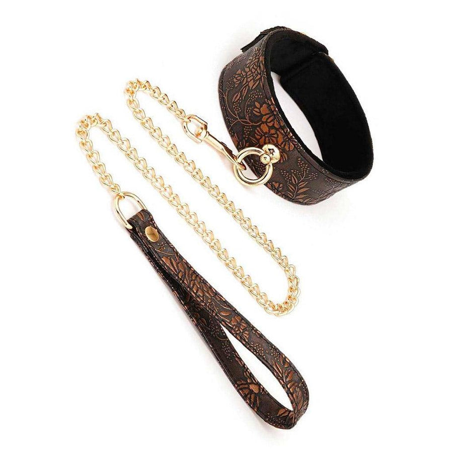 The Vegan Floral Collar With Faux Fur And Leash Set is displayed against a blank background. The collar is brown with an ornate floral pattern on it and gold hardware, including an O-ring. The included gold chain leash with a matching handle is clipped to the O-ring.