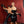 Load image into Gallery viewer, A woman stands in the foreground, wearing a black latex Newmar Dress with a matching waist cincher and gloves, holding the 24&quot; Basic Suede Flogger in both hands. Behind her is a man wearing black latex jeans leaning on a St. Andrews cross.
