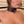 Load image into Gallery viewer, A close-up of a nude woman’s torso is shown in front of a beige wall. The adjustable black leather collar of the Adjustable Yoke is secured around her neck with a padlock. Behind her neck, the black rod of the yoke extends horizontally.
