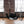 Load image into Gallery viewer, The black Leather Sling with metal rivets is suspended from the ceiling by chains in a brick room. It has a large central piece and two smaller leather pieces for suspension on top and bottom. Stirrups hang from the chains at the bottom of the swing.
