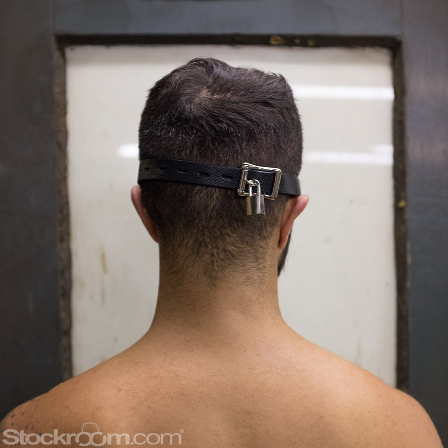 A closeup of the back of a dark-haired man’s head is shown. He is wearing the Adjustable Aviator Blindfold, which is buckled around his head. The buckle is silver and is locked with a small silver padlock.