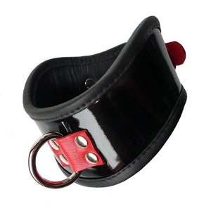 The Firecracker Patent Leather Posture Collar is shown against a blank background. The collar is patent leather with matte black leather lining. A piece of red leather secures a metal D-ring in the front.