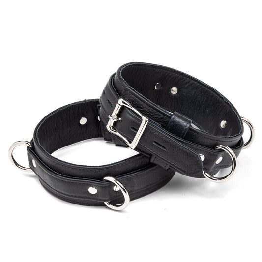 The Premium Garment Leather Locking Thigh Restraint set in black is displayed against a white background. It is a thick band of black leather with silver metal hardware. The cuff has three evenly spaced D-rings.