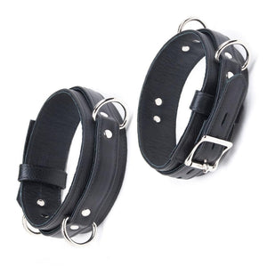 The Premium Garment Leather Locking Thigh Restraint set in black is displayed against a blank background. It is a thick band of black leather with silver metal hardware. The cuff has three evenly spaced D-rings.