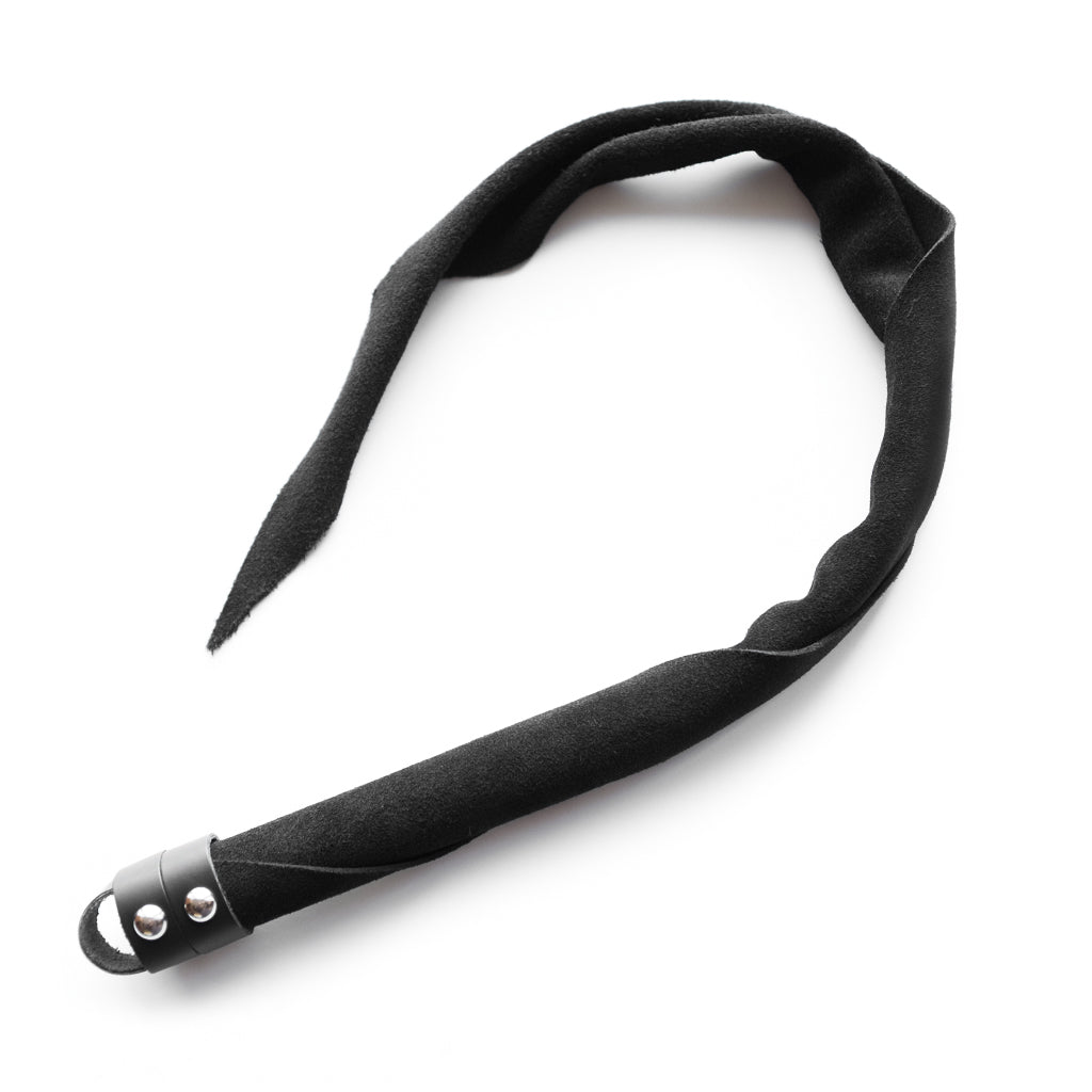 The Black Suede Dragon Tail Whip is shown against a blank background. The suede is wrapped around itself in a tight cylinder at the handle, which loosens towards the top and comes to a point. 