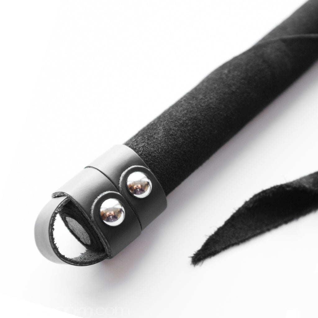 A close-up of the handle of the Black Suede Dragon Tail Whip is shown against a blank background. There is a small leather loop at the base of the handle.
