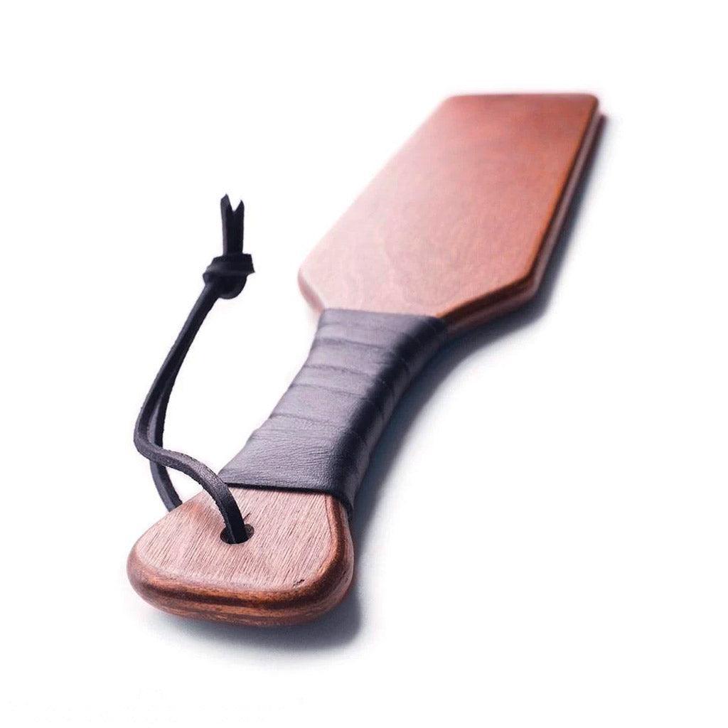 A closeup of the handle of the Leather Wrapped Wood Spanking Paddle is shown against a blank background.