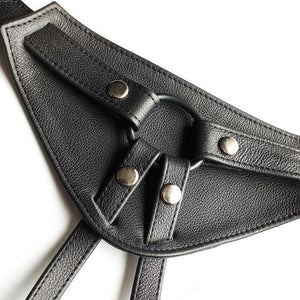 A close-up of the front piece of The Full Curves Leather Strap-on Harness in black is displayed against a blank background. 