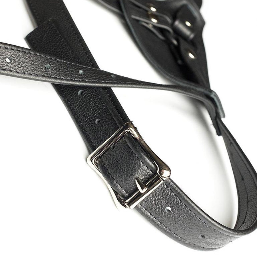 A close-up of the straps on The Full Curves Leather Strap-on Harness in black is displayed against a blank background. The straps are adjustable and are fastened with metal buckles.