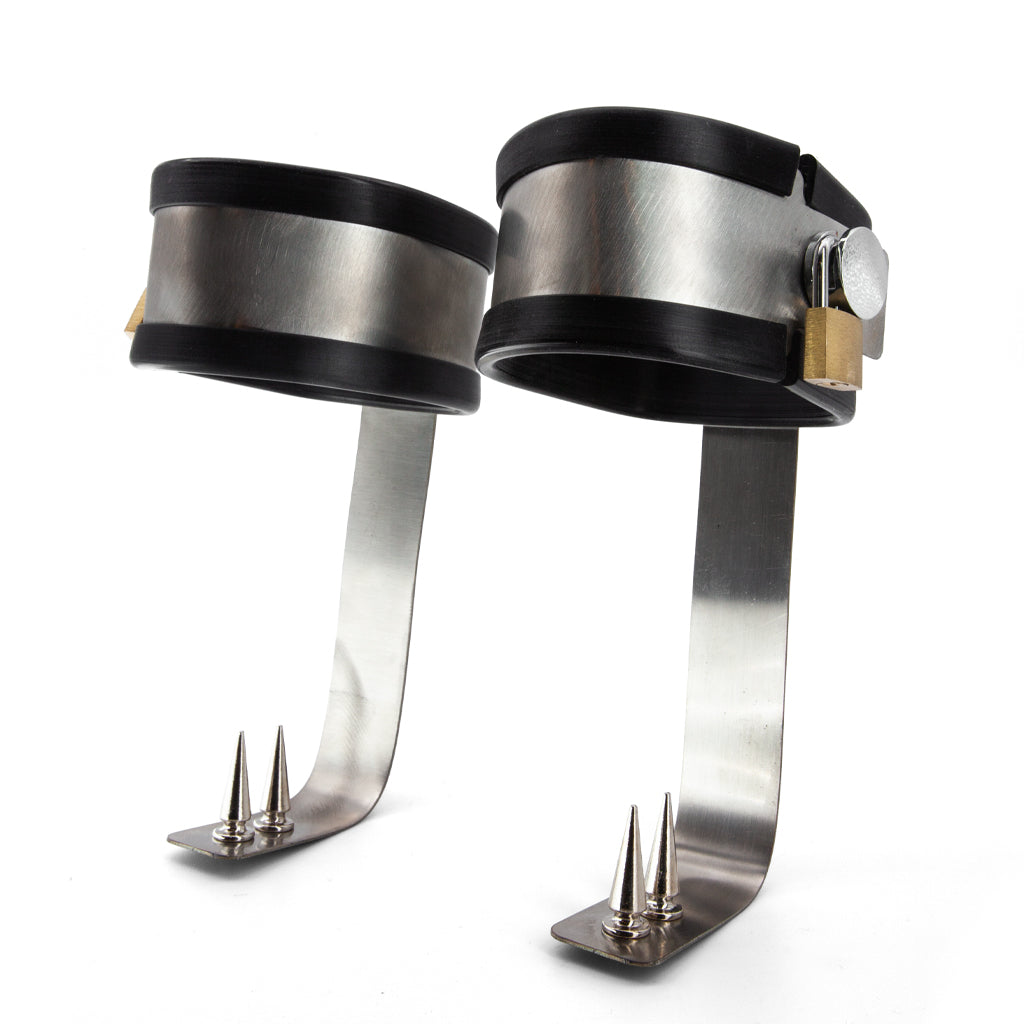 Two metal ankle restraints on a white background. The cuffs have long metal extensions with spikes for the bottom of the feet. 