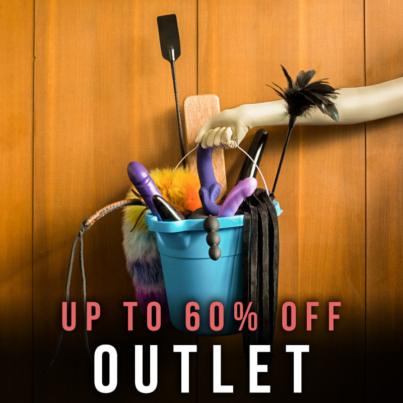 Text: “Outlet. Up to 60% Off”  Black and white photo with a view over a table which has a whip, spreader bar with cuffs, a riding crop, and other BDSM gear. On the far side, a young white woman stands with her backside to the camera, wearing black latex underwear with garters and latex stockings.