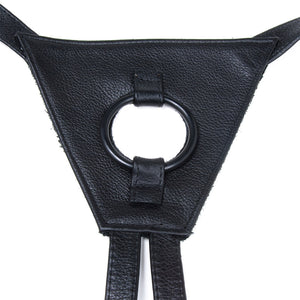 A close-up of the front piece of the Texas Two-Strap strap-on harness is shown against a blank background. The front piece is triangular and has a black silicone O-ring in the middle.