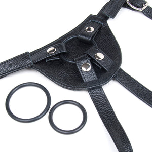 A close-up of the front of the Terra Firma black Leather Strap-on Harness is displayed against a blank background. The three different-sized silicone O-rings that the harness comes with are also shown.