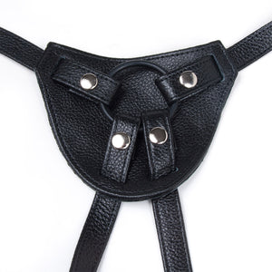 A close-up of the front piece of the Terra Firma Dee Black Leather Strap-on Harness is shown against a blank background. The harness has a black silicone O-ring which is held in place by snap-closures on the hip and leg straps.