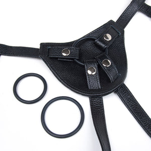 A close-up of the front piece of the Terra Firma Dee black Leather Strap-on Harness is displayed against a blank background. The three different-sized silicone O-rings that come with the harness are shown.