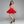 Load image into Gallery viewer, A dark-haired woman is posed in front of a grey backdrop. She wears a translucent pink latex camisole and a red latex Cheerleader Skirt from Syren latex, as well as black high heels.
