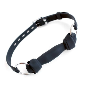The Silicone Bone Gag with a Silicone Strap is shown against a blank background. The gag resembles a dog bone with knotted ends. It is attached to an adjustable silicone strap with metal O-rings.