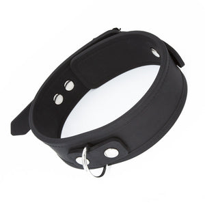 The Silicone Locking Collar is displayed against a blank background. It is made of a relatively wide piece of matte black silicone with faux stitching along the borders. It has a metal D-ring at the front and decorative metal rivets.
