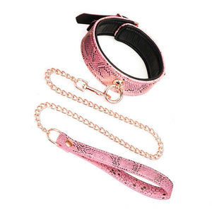 The Rose Gold Snake Collar And Leash Set is displayed against a blank background. The collar has a pink snakeskin design with a rose gold O-ring in the front. The included rose gold chain leash with a pink snakeskin handle is attached to the O-ring.