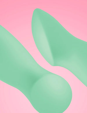 A closeup of two Fun Factory Sundaze Pulsating Vibrators in Pistachio are shown against a pink background, displaying the contours of the tip of the toy. 