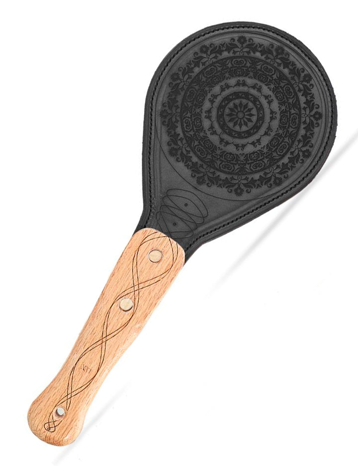 The LVX Floral Leather Paddle is displayed against a blank background. The handle of the paddle is a light colored wood with a darker swirling design. The upper portion of the paddle is black leather decorated with an intricate floral design.