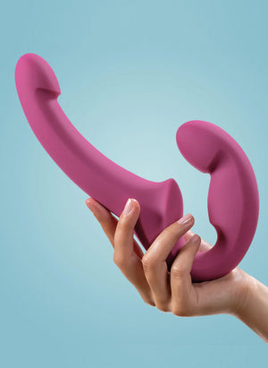 A woman’s hand is shown holding up a Fun Factory Share Lite Double Dildo in Blackberry against a light blue background.