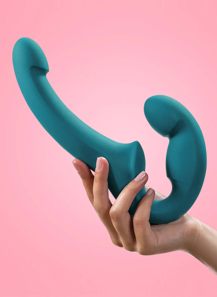 A woman’s hand is shown holding up a Fun Factory Share Lite Double Dildo in Deep Sea Blue against a pink background.