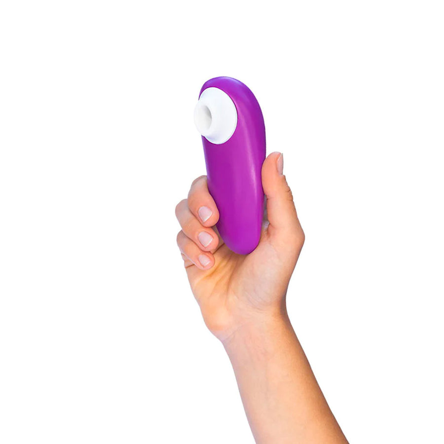 A hand is shown holding a Womanizer Starlet 3 vibrator in Violet up against a blank background.