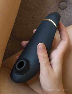 A closeup shot of a naked woman holding a black Womanizer Premium 2 near her vagina.
