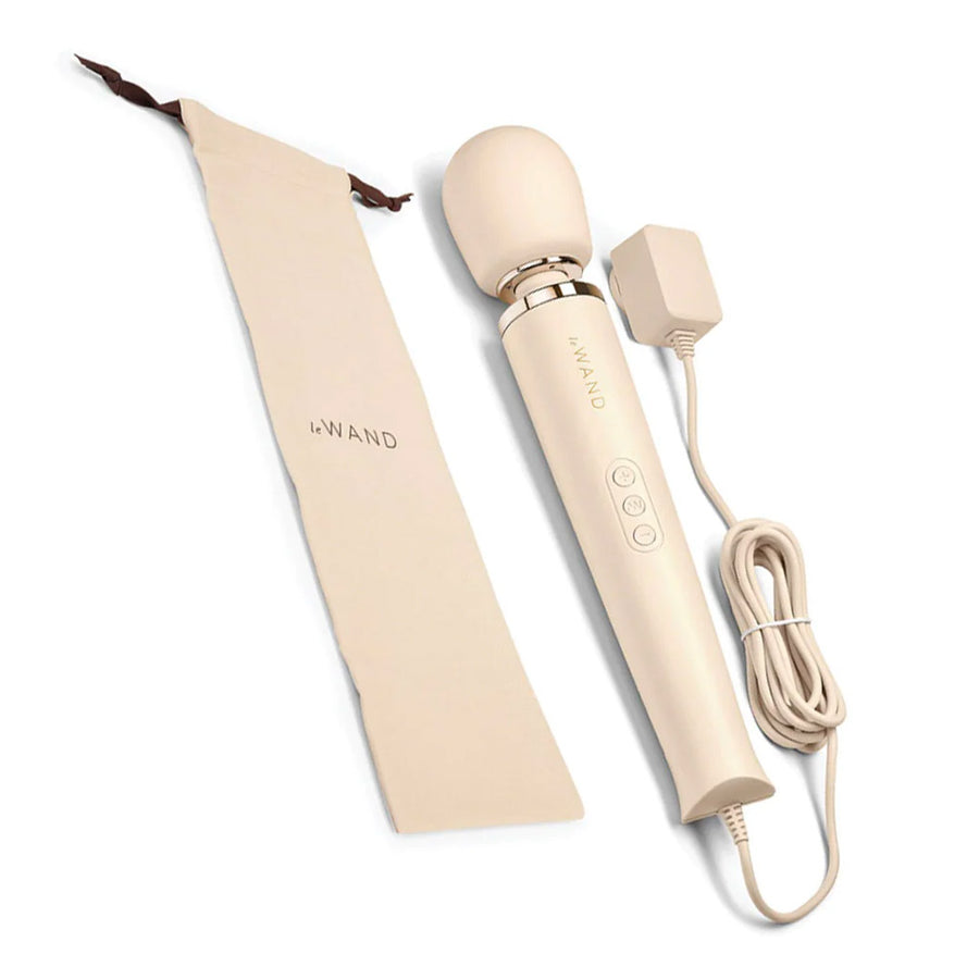A Le Wand Plug-In Vibrating Massager in Cream is shown against a blank background with its cord coiled next to it and its storage bag on the other side.
