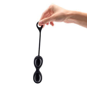 A hand is shown holding the Black Obsidian Le Wand Crystal Yoni Eggs in their silicone case in front of a blank background.