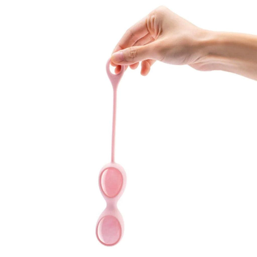 A hand is shown holding the Rose Quartz Le Wand Crystal Yoni Eggs in their silicone case in front of a blank background.
