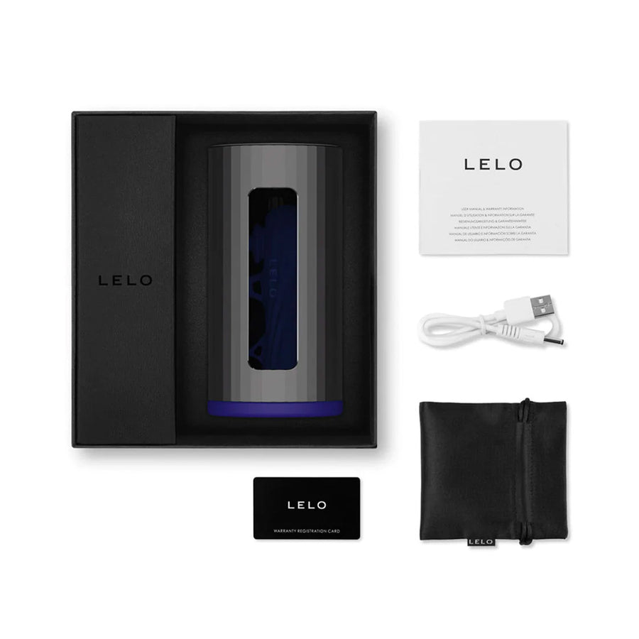 The contents of the Lelo F1S V2X Vibrating Masturbator packaging are shown against a blank background. Displayed are the masturbator in its box, a charger, a case for the charger, an instruction manual, and a warranty information card.