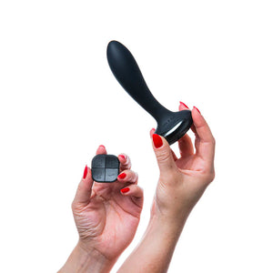 A woman’s hand with red nailpolish is shown holding up the Hot Octopuss Plex With Flex Vibrating Anal Butt Plug in one hand and the remote in the other against a blank background.