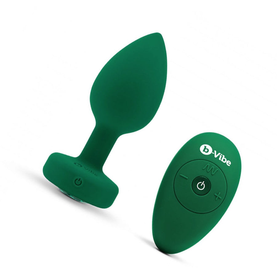 The b-Vibe Vibrating Jewel Butt Plug is shown against a blank background next to its 4 buttoned remote. The plug is a size M/L, which is Emerald colored. 
