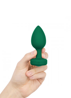 A hand is shown holding up the b-Vibe Vibrating Jewel Butt Plug in Emerald against a blank background.